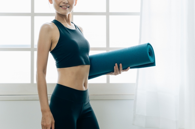 ピラティスマットを抱えてピラティスを始める準備をしている女性