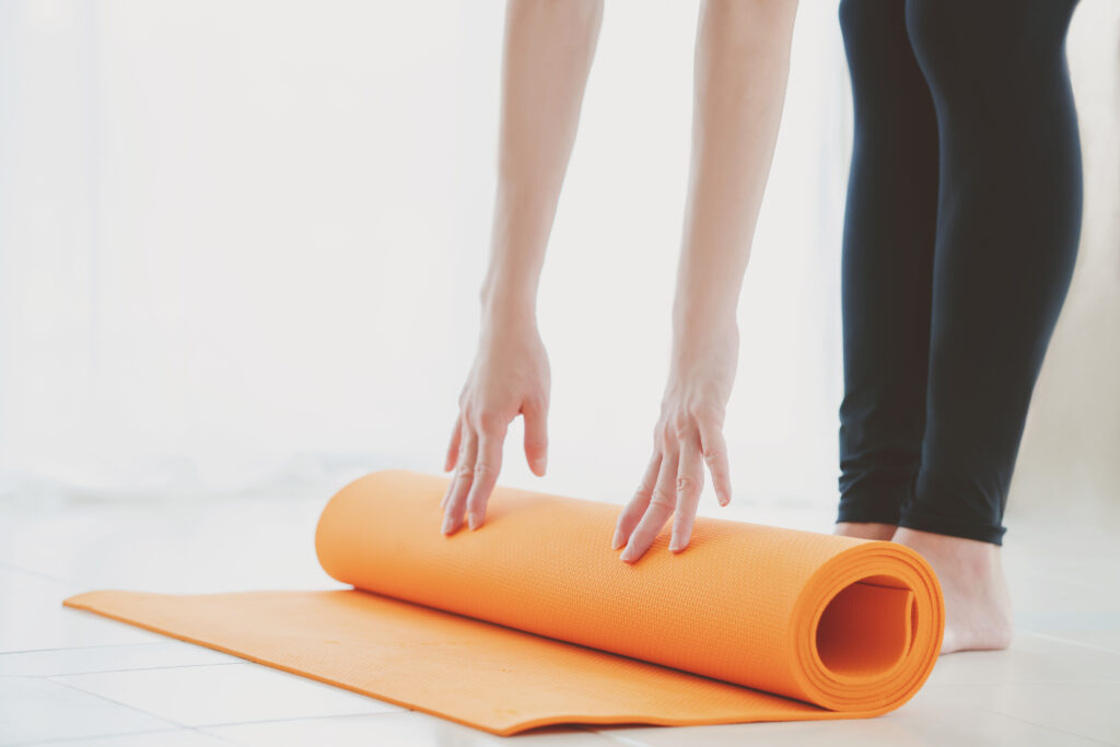 ウォールピラティスや体幹トレーニングを始めるために、明るい部屋でヨガマットを広げる女性