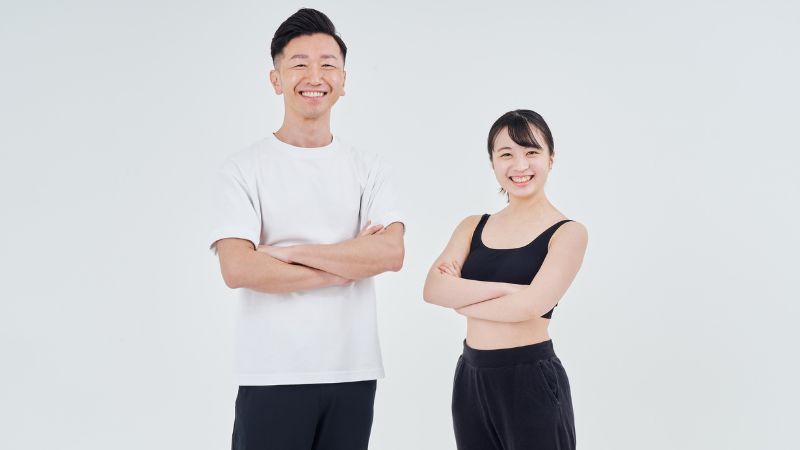 明るいスタジオで腕組みをして微笑む、ピラティス指導を行うインストラクターの男女2人