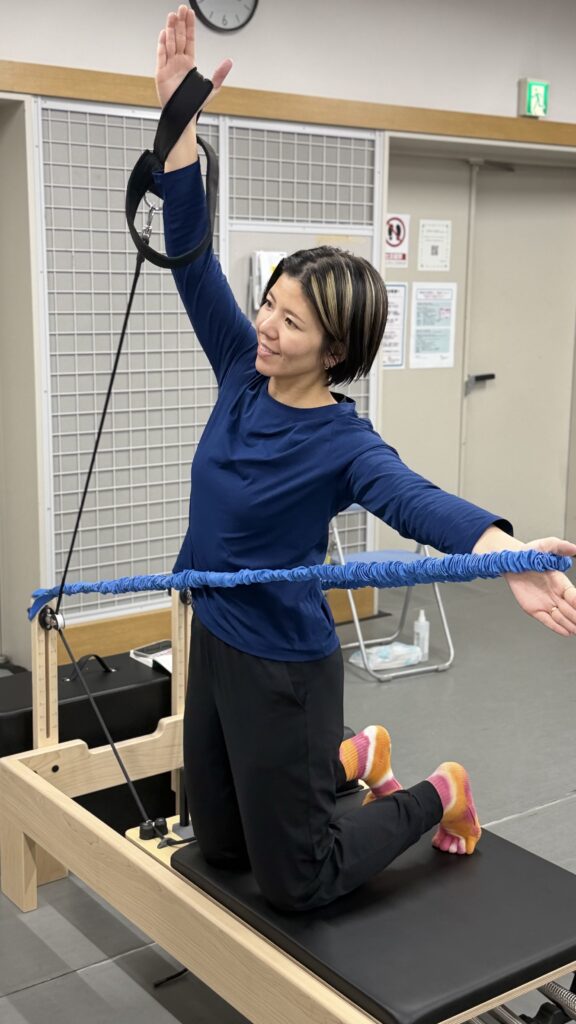 日本人のピラティスインストラクターがリフォーマー上でコネクションズバンドを活用してエクササイズをしている画像