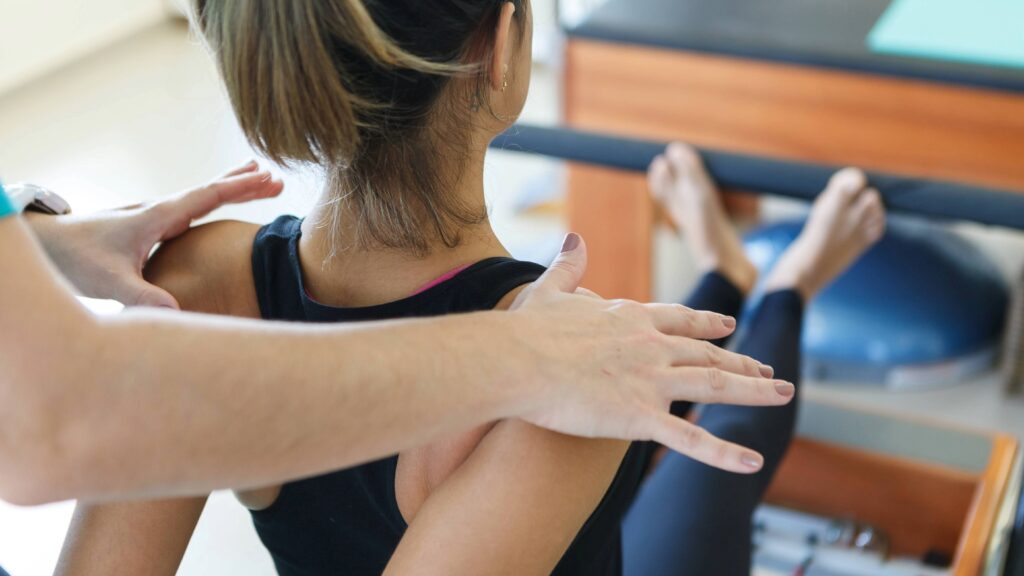 背を向けた受講者の女性に対し、インストラクターが両手を肩に添えて、姿勢の補助や調整を行っているクローズアップ。