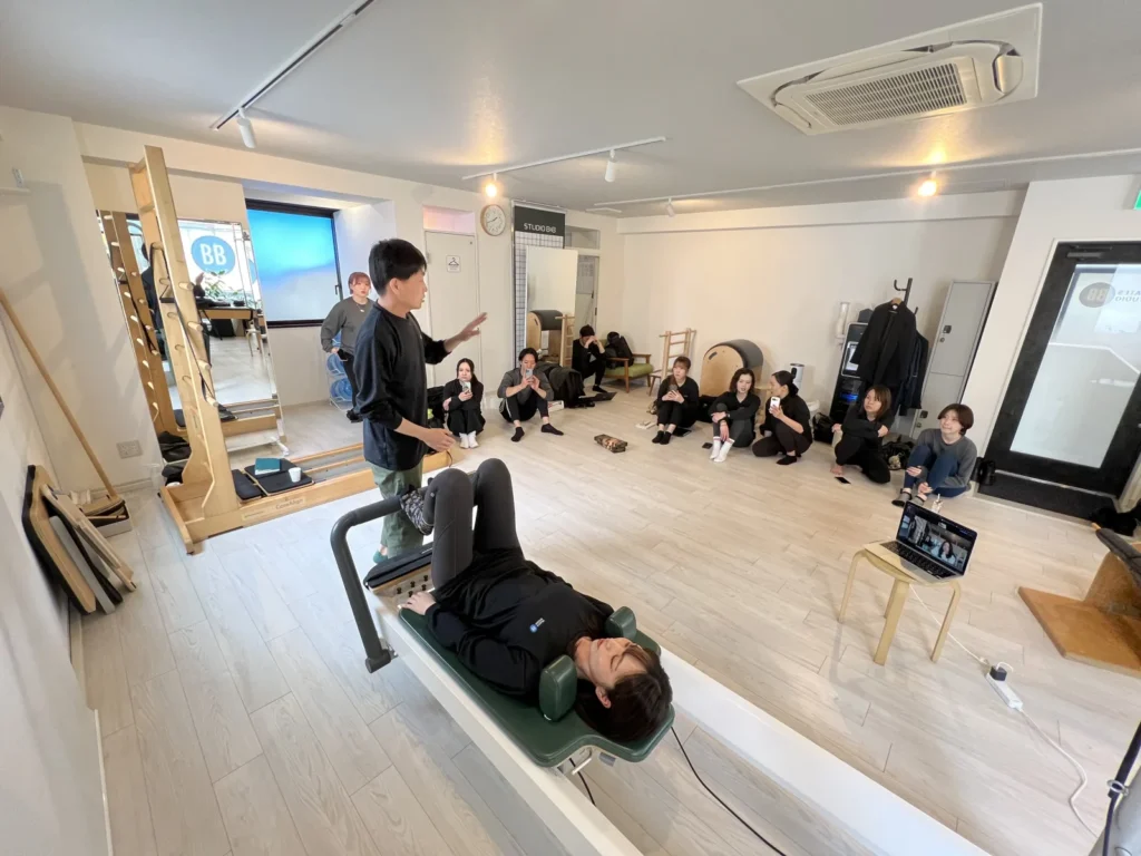 ピラティススタジオBBの社内全体ミーティングで先輩が研修を行う風景。知識ゼロからプロになるための研修体制を示す。