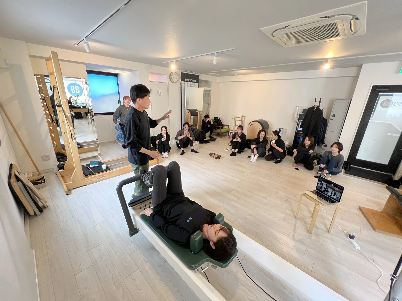 ピラティススタジオBBの社内全体ミーティングで先輩が研修を行う風景。知識ゼロからプロになるための研修体制を示す。